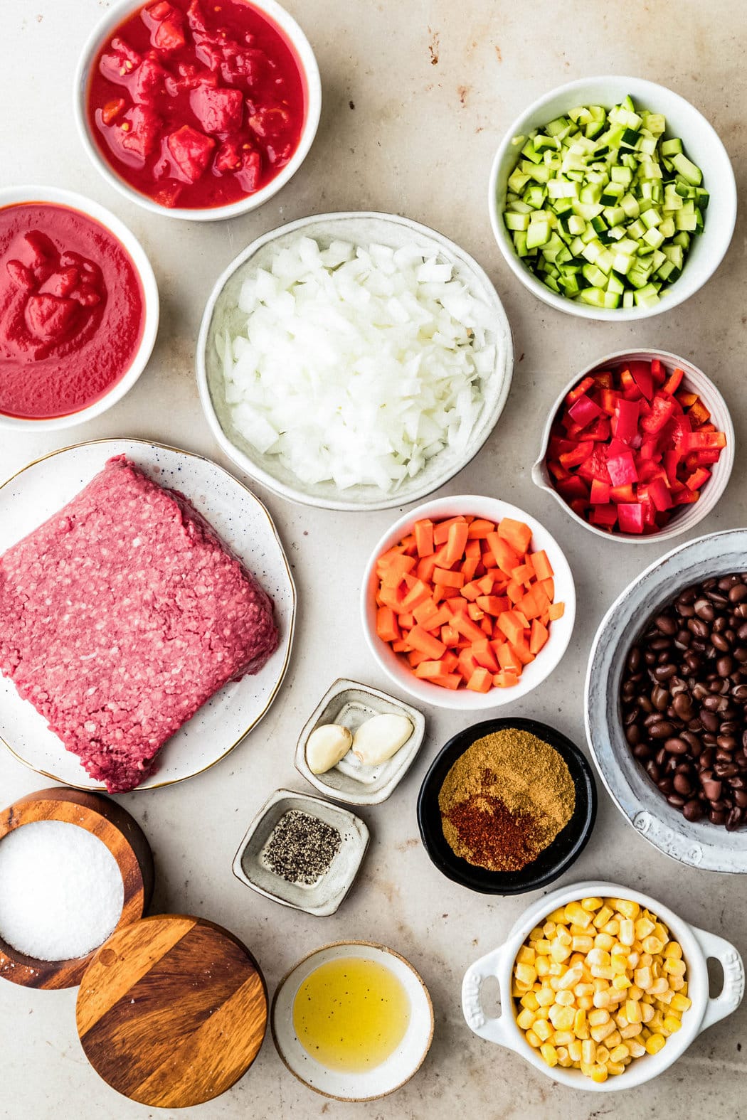 Overhead view of dishes containing the individual ingredients for turkey chili, including  lean ground turkey, zucchini, black beans, garlic, onions and more. 