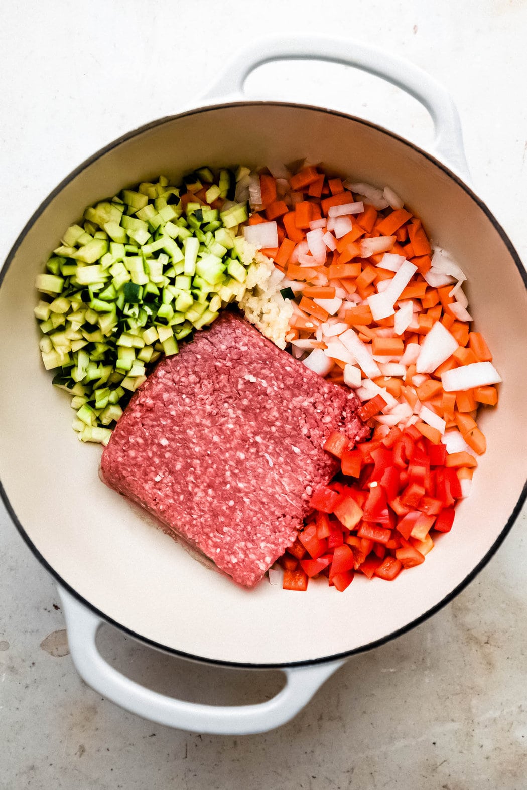 Ground turkey, onions, carrots, bell peppers, garlic, and zucchini about to be sautéed in a large Dutch oven for turkey chili. 