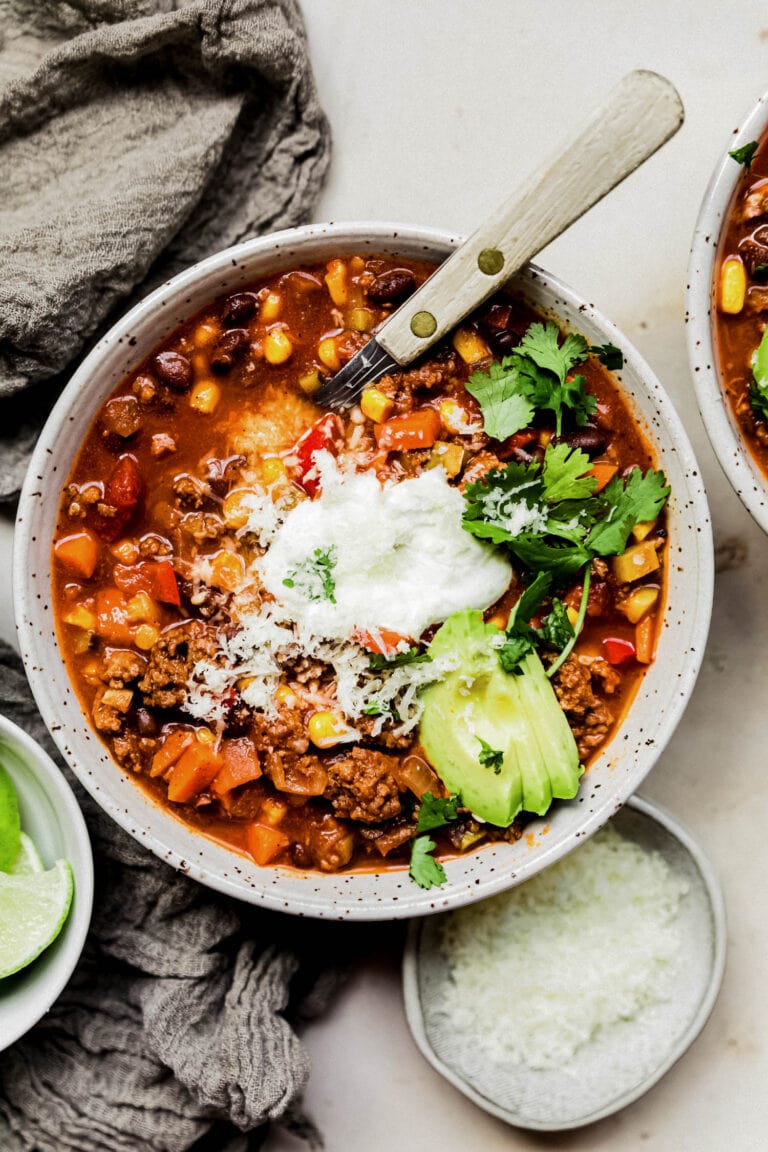 Overhead view of a white bowl of healthy turkey chili topped with sour cream, avocado, and cilantro. 