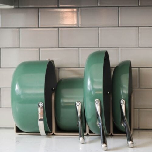 A set of green Caraway pots and pans in magnetic holder on countertop