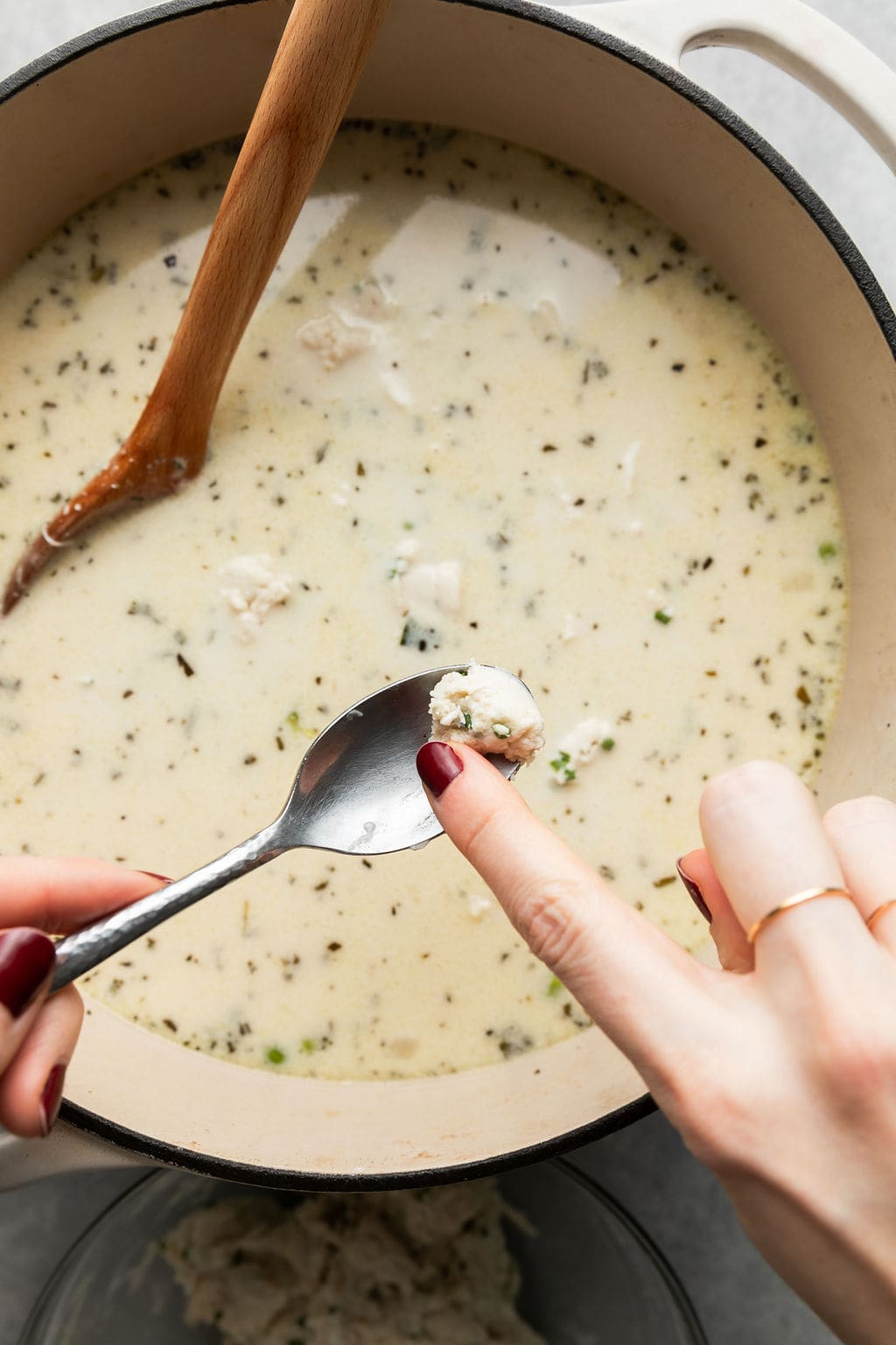 An overhead view of a raw dumpling dough piece being dropped into a pot of Chicken Dumpling soup. 