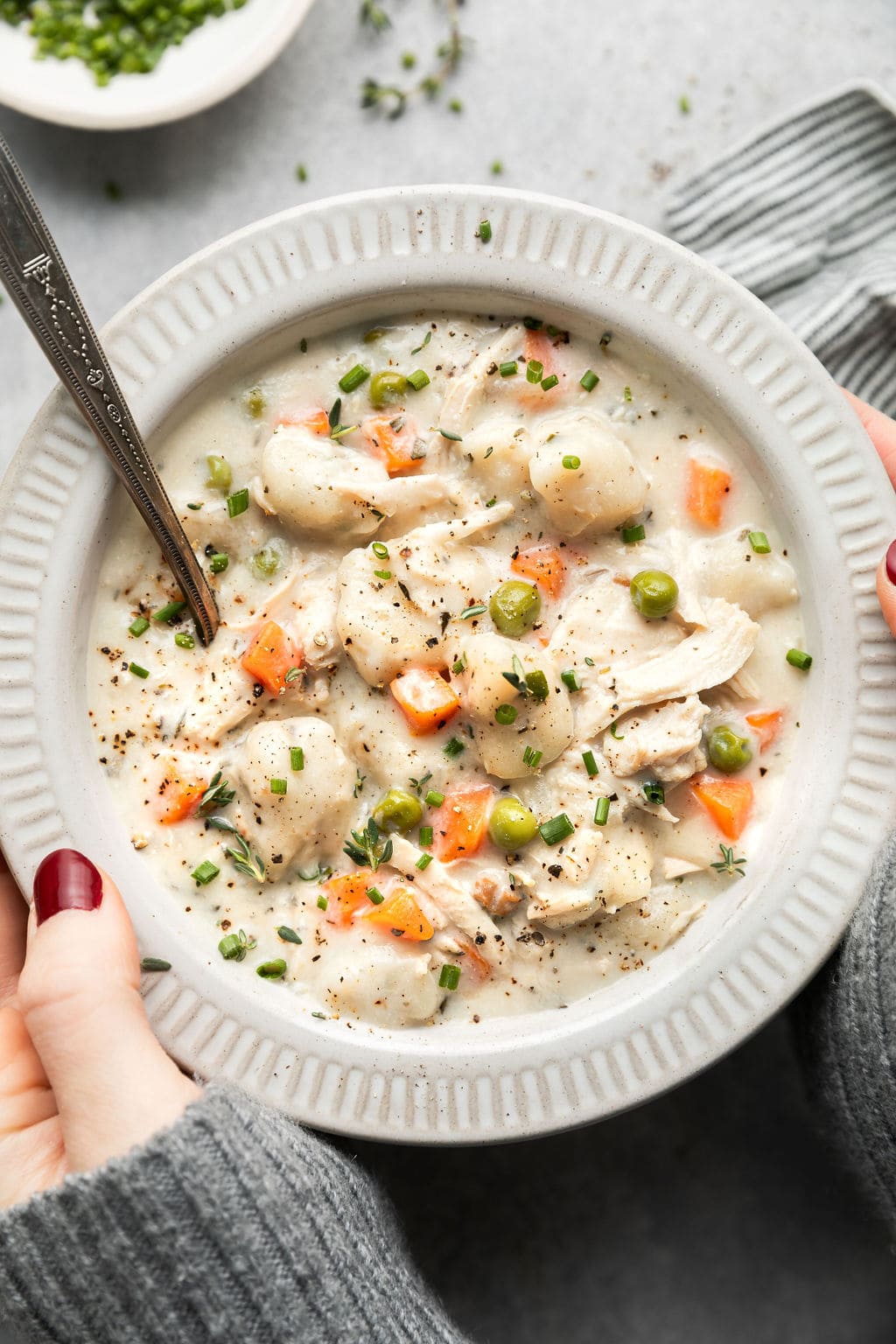 A close up of a bowl of Chicken Dumpling soup showing off the tender chicken, delicious dumplings, and peas and carrots. 