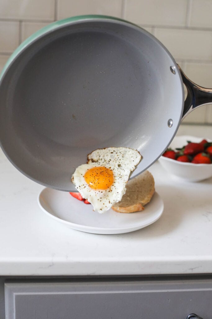 A fried egg sliding out of Caraway skillet onto white plate
