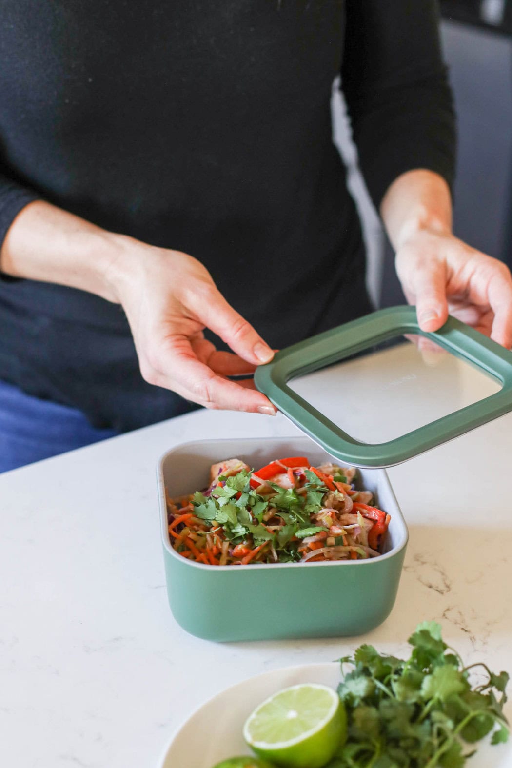 Close up view of someone putting a lid on a caraway storage container filled with pad thai. 