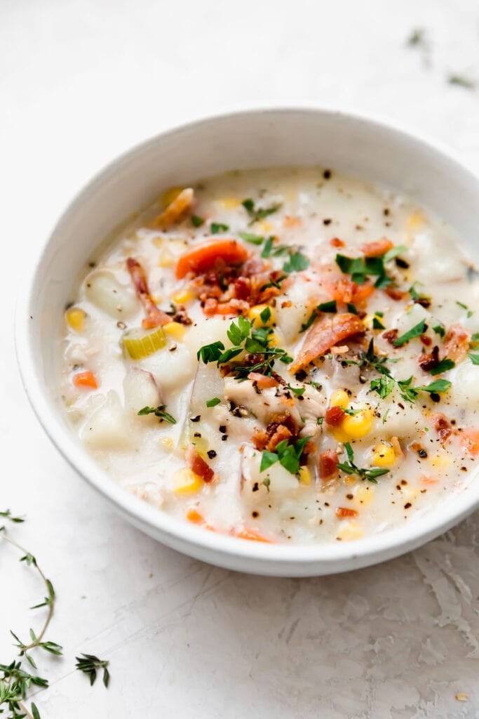 Creamy chicken corn chowder in white bowl topped with crisp-cooked bacon and chopped fresh herbs