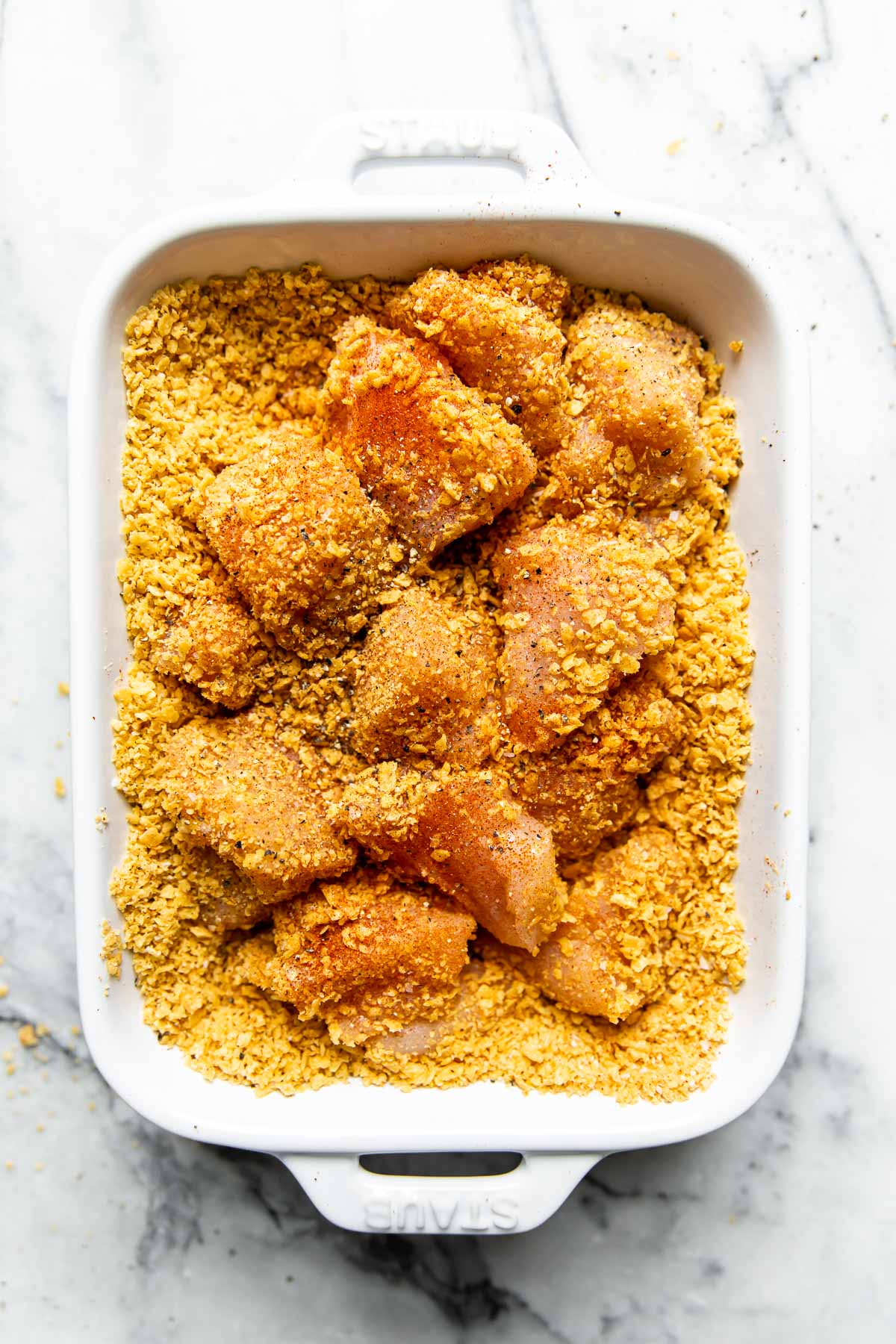Overhead view chicken pieces in crushed corn tortilla chip mixture for a breading for homemade chicken nuggets.