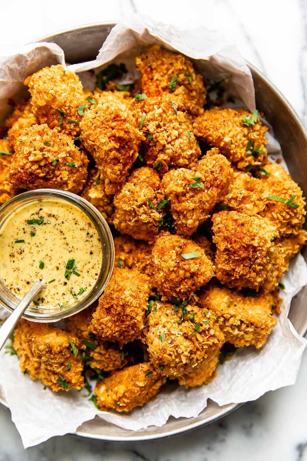 A tin serving dish piled with golden brown chicken nuggets with a small container of honey-mustard dipping sauce. 