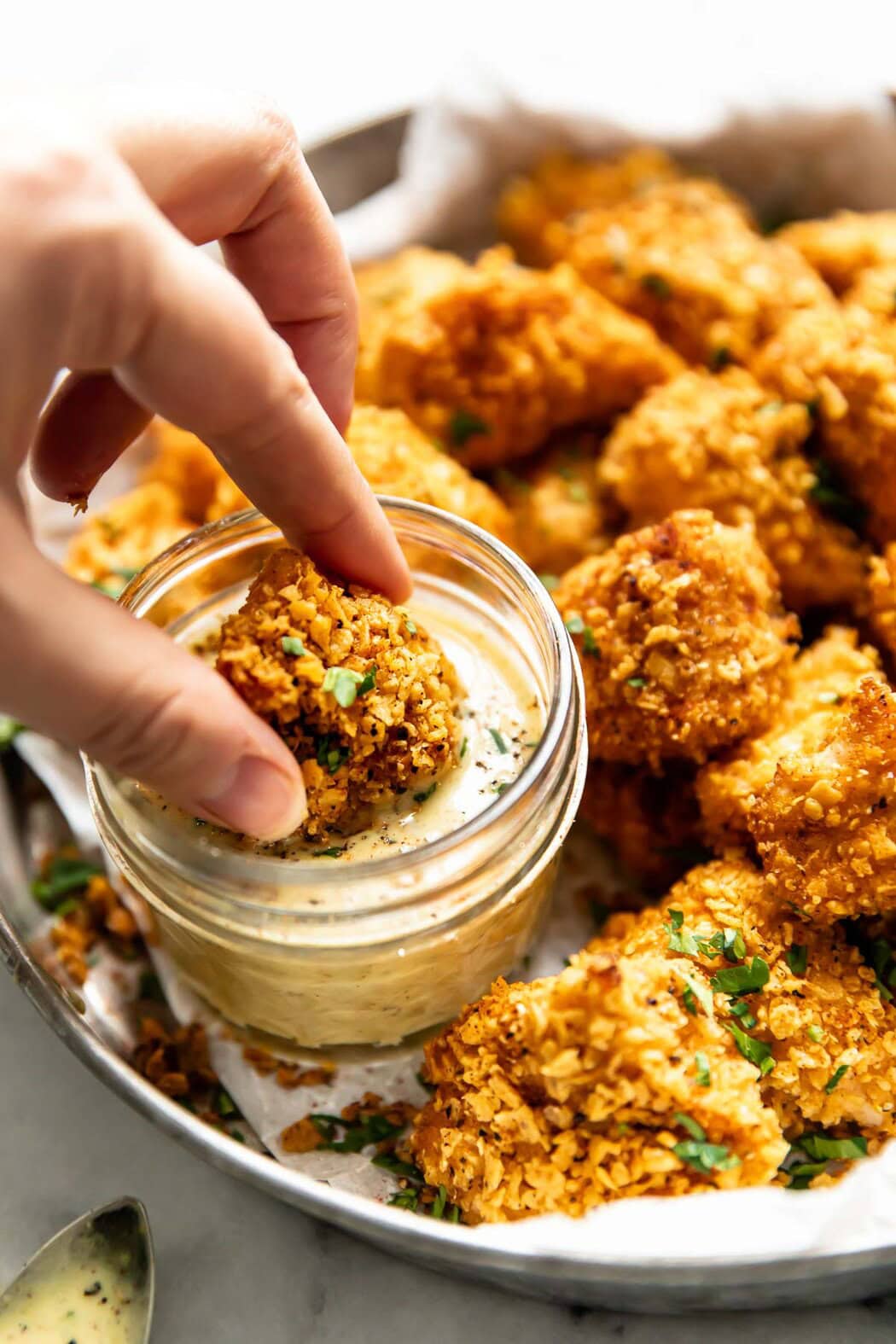 A homemade breaded chicken nugget being dipped into small jar of honey mustard sauce.