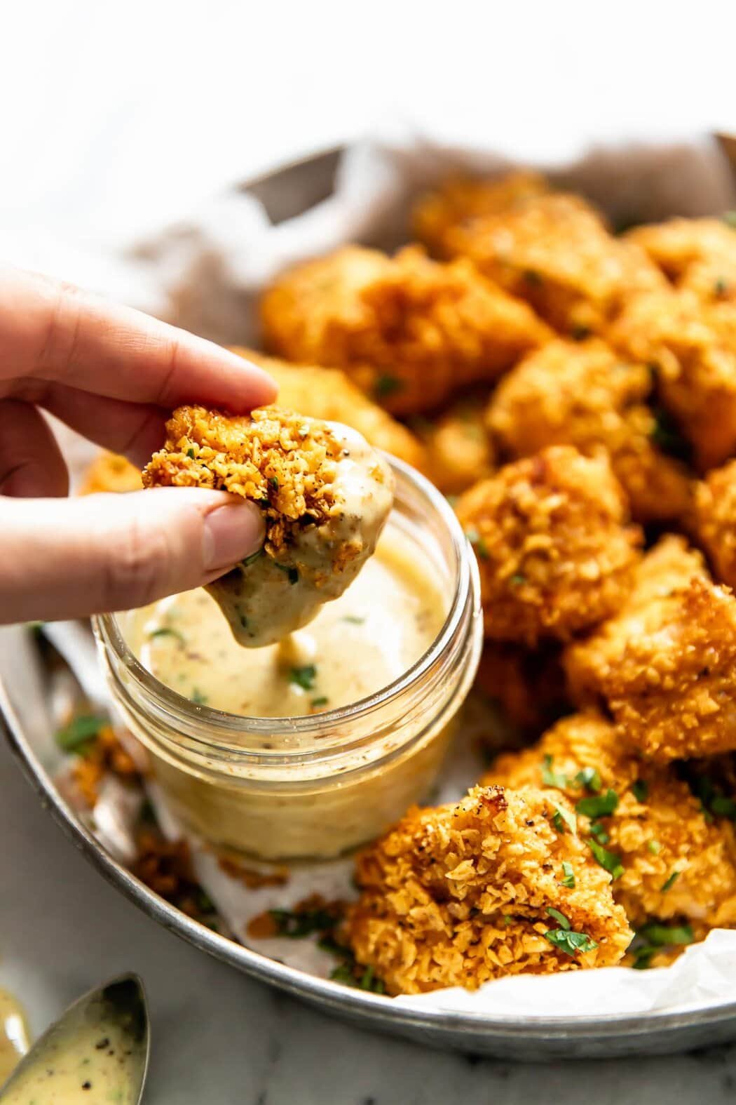 A homemade chicken nugget being dipped in small jar of honey mustard sauce.
