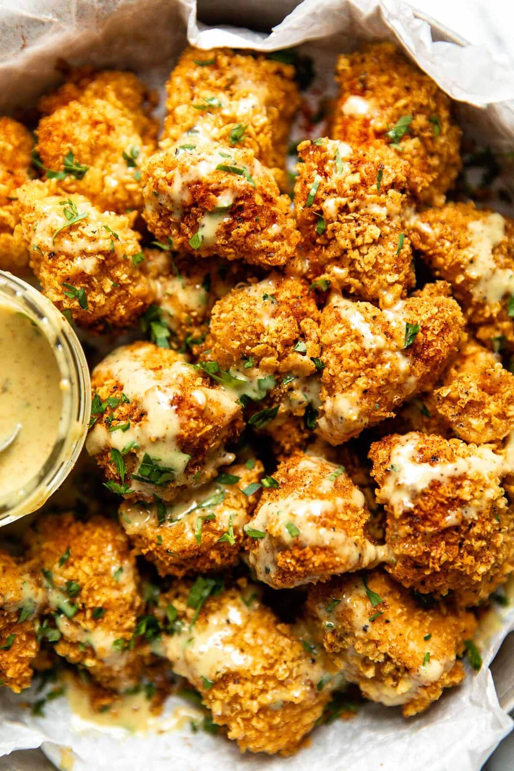 A close up of crispy homemade chicken nuggets drizzled with a honey-mustard sauce. 