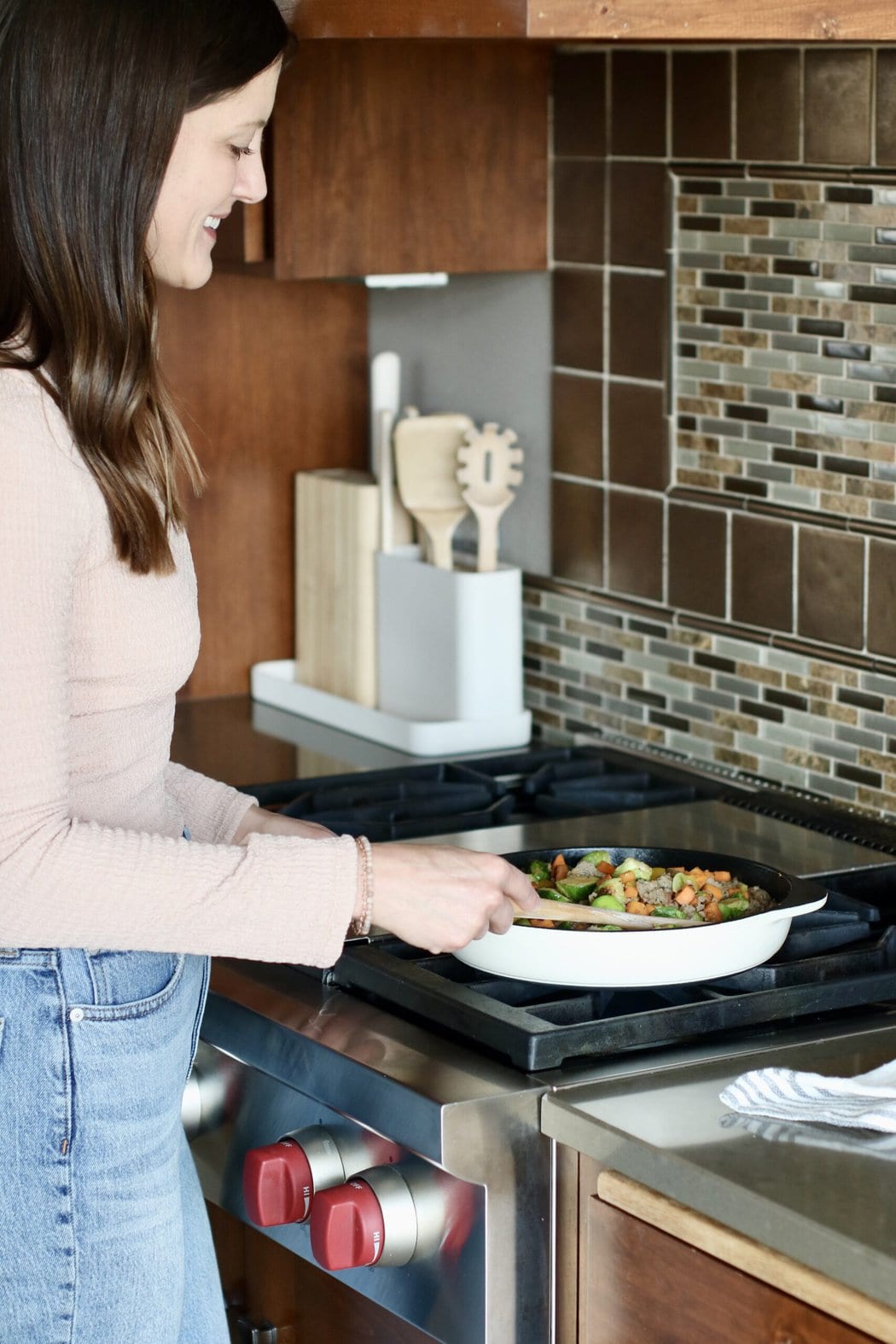 Woman standing over a stove top using a caraway skillet. 