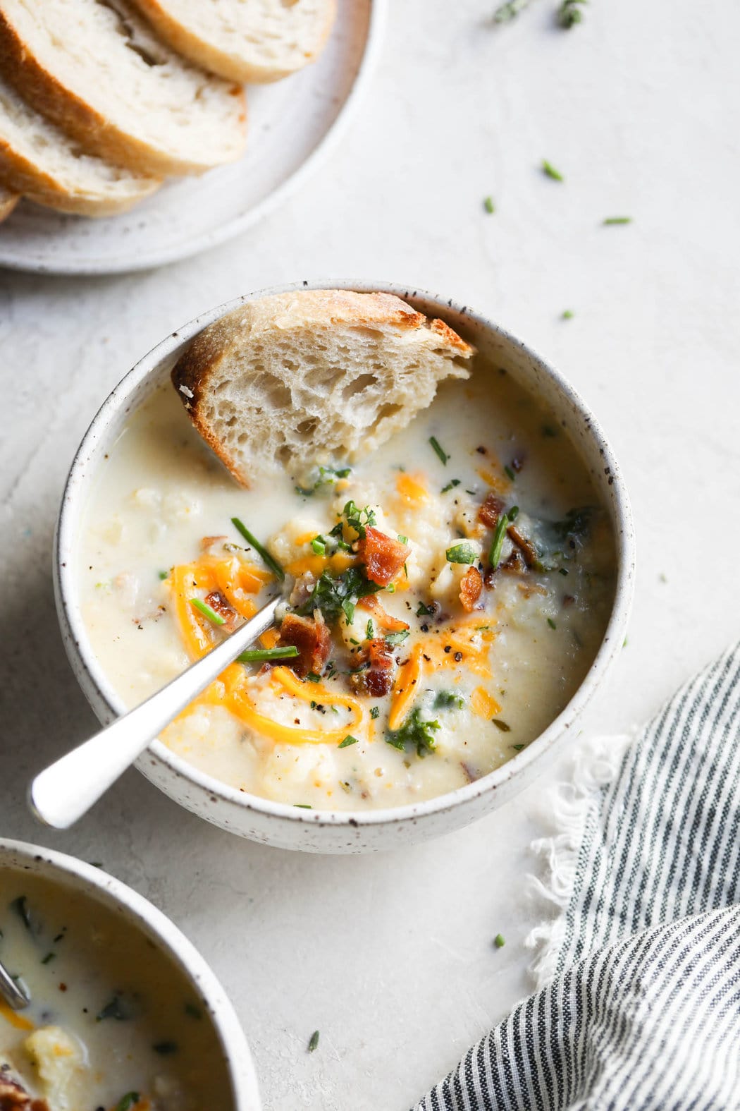 Aerial view of Loaded Cauliflower Soup topped with shredded cheese, bacon, herbs, and a fresh slice of bread. 