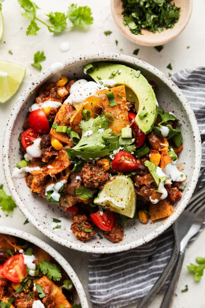 Beef skillet enchiladas plated in a stone bowl topped with avocado slices, sour cream and fresh cilantro