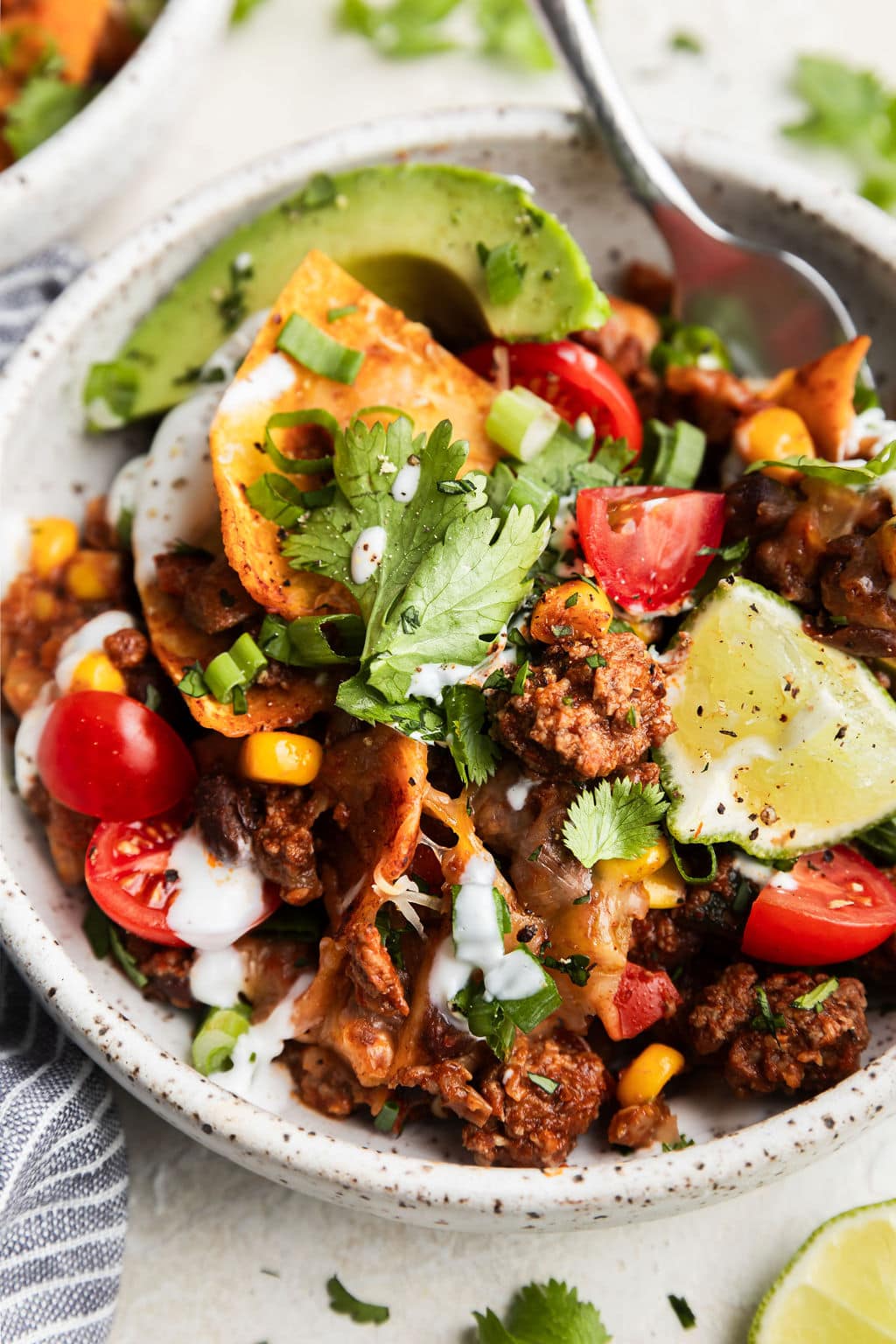 Beef skillet enchilada served in bowl; close up shot of ground beef, black beans, and corn coated in enchilada sauce topped with taco toppings