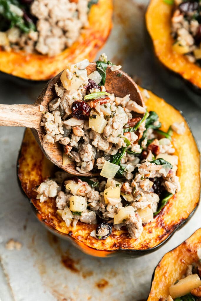 A spoonful of sausage, apple, spinach and Parmesan stuffing being filled into acorn squash half