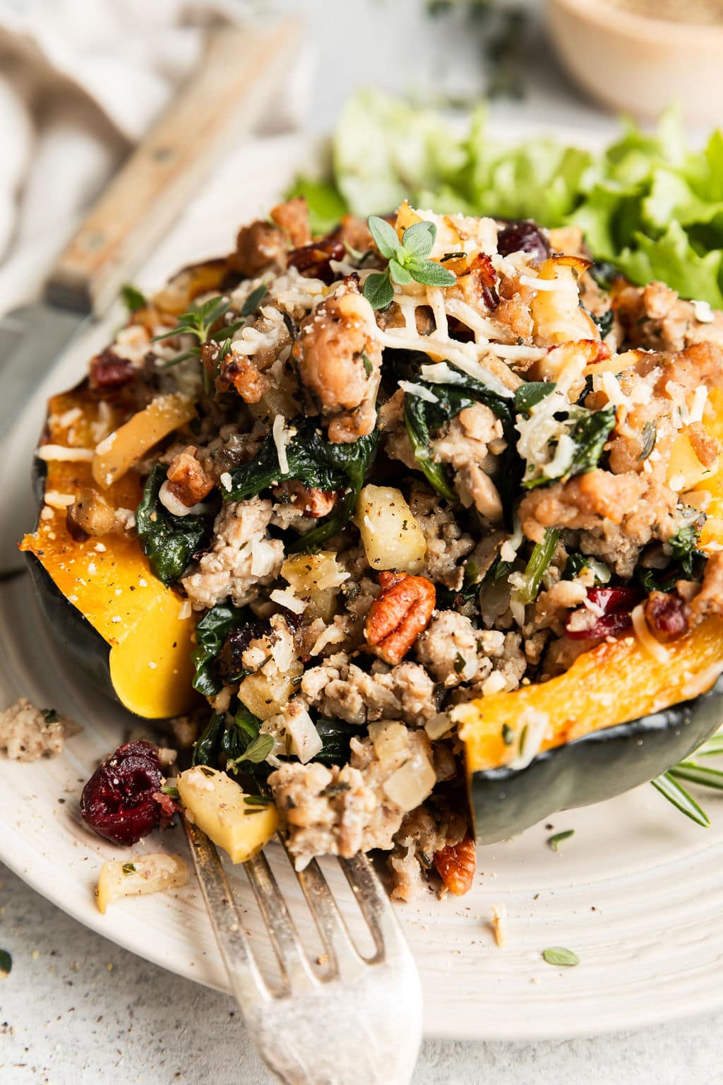 Side view sausage stuffed acorn squash half topped with Parmesan and fresh herbs