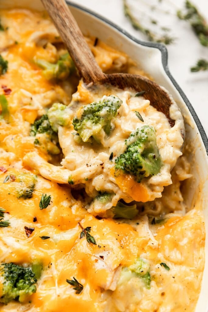 A wooden spoon scooping up spoonful of cheesy chicken, broccoli, rice mixture from skillet