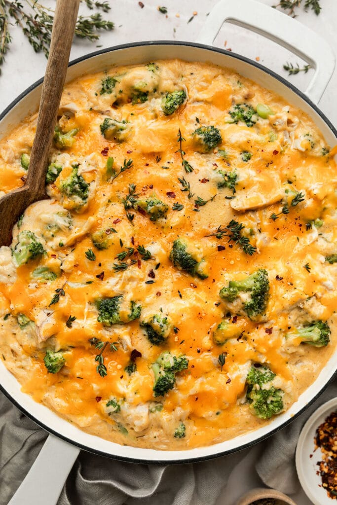 Overhead view skillet filled with cheesy chicken and rice with broccoli, melted cheddar cheese on top