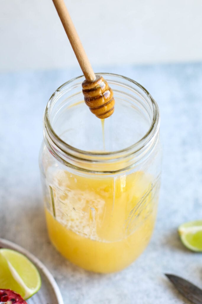 Honey being drizzled from honey dipper into mason jar with margarita mix ingredients