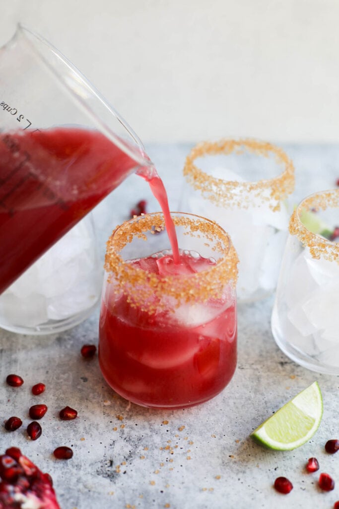 Pomegranate margarita being poured into short glass with coarse sugar coating glass rim.