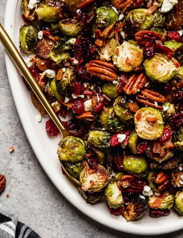 Roasted Brussel Sprouts with Bacon and Balsamic on a white serving platter with a gold serving spoon.