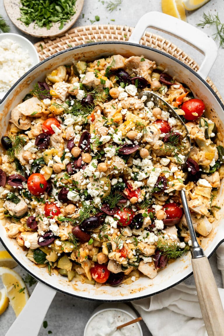 Overhead view white skillet filled with Greek Orzo with chicken and chickpeas, topped with feta cheese and kalamata olives.