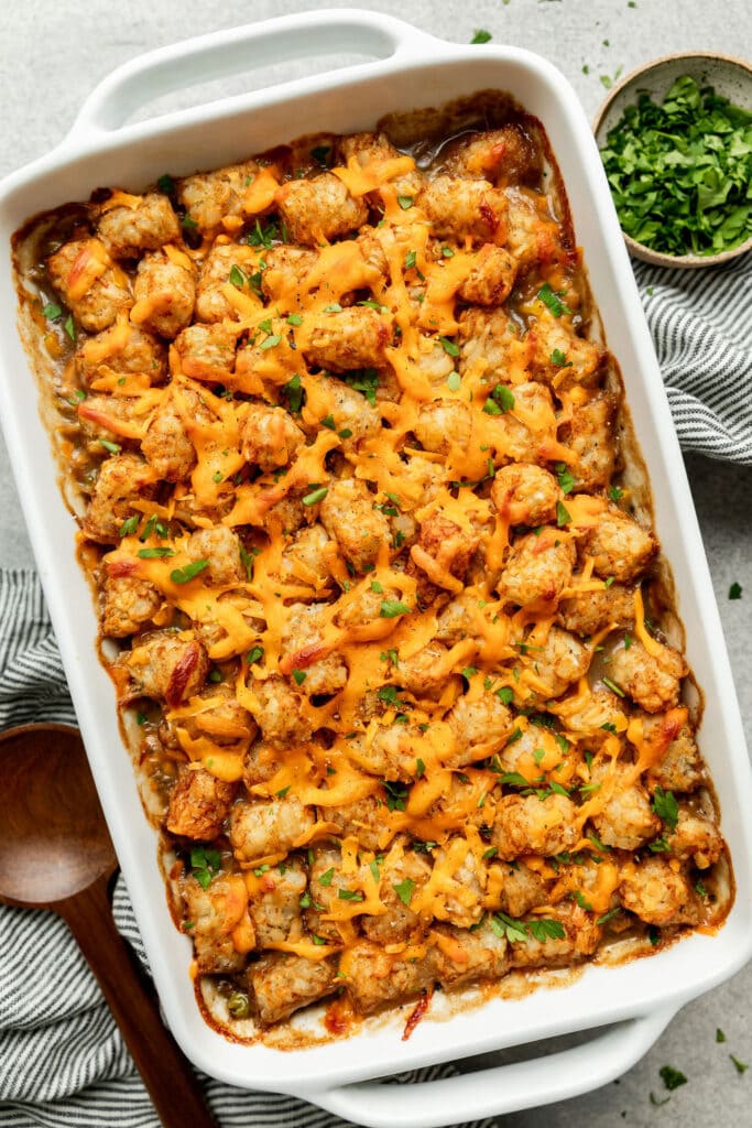 Overhead view of white baking dish filled with freshly baked tater tot casserole complete with melted cheese and fresh herbs on top. 