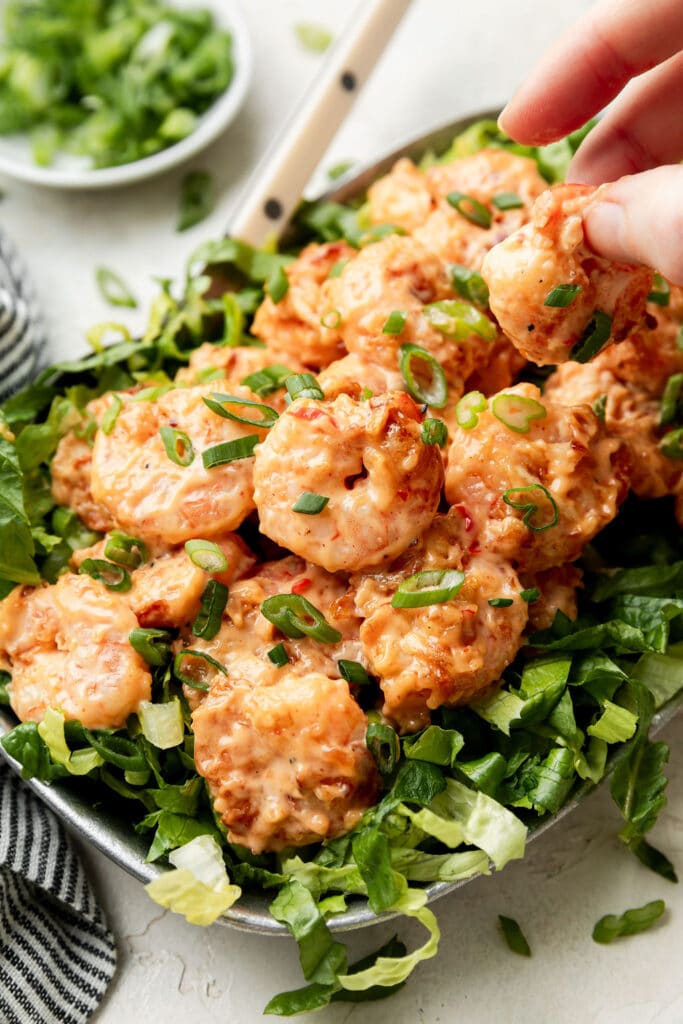 Close up view of Bang Bang Shrimp on top of lettuce topped with sliced green onions. 