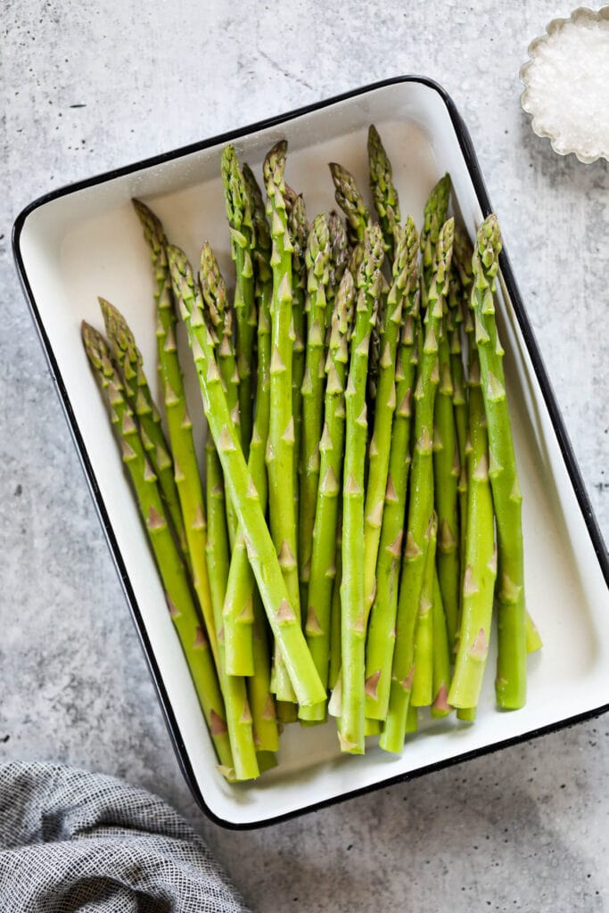 Overhead view of freshly cut asparagus stalks in a white baking dish. 