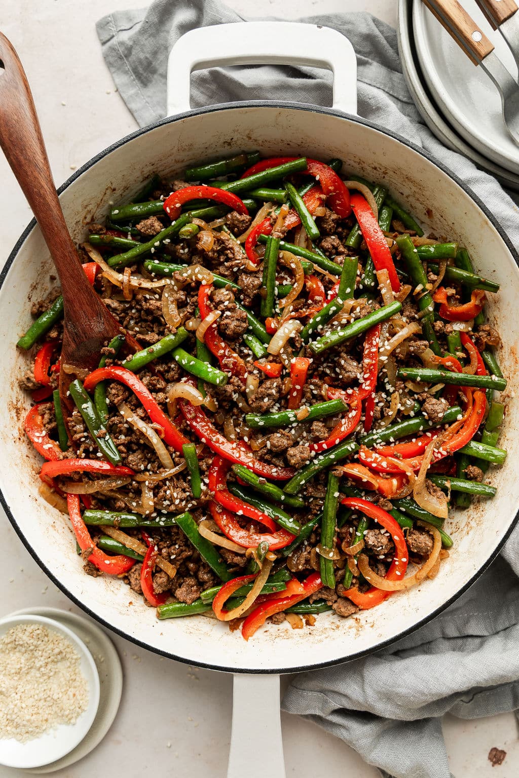 Close up view of Ground Beef Stir Fry in white skillet being stirred with a wooden spoon.