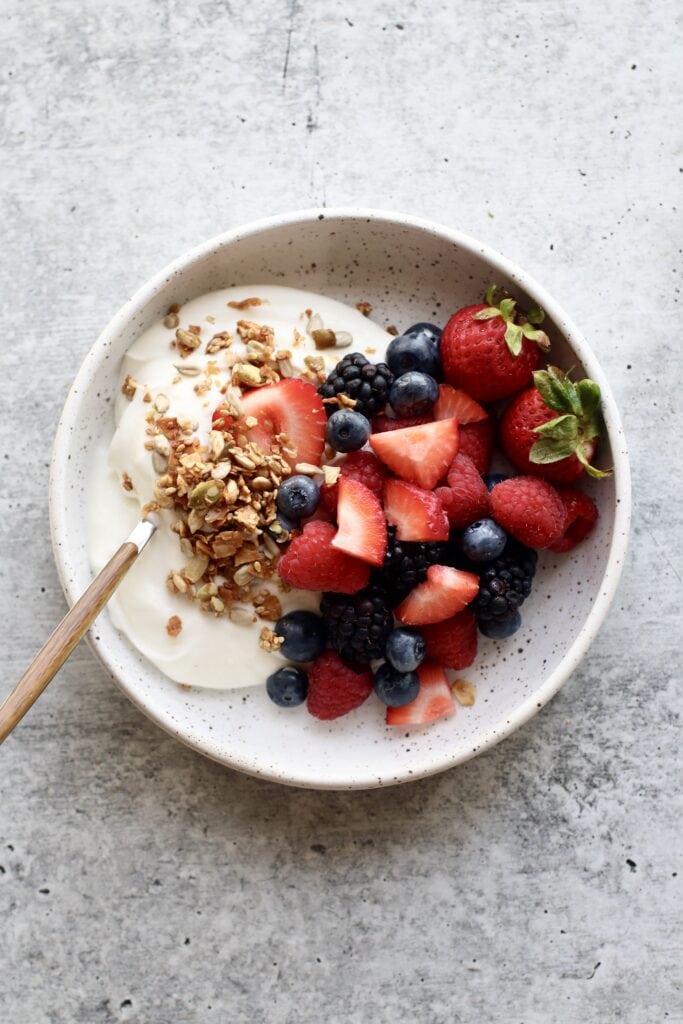 Overhead view of a white bowl filled with yogurt, fresh fruit, and granola. 