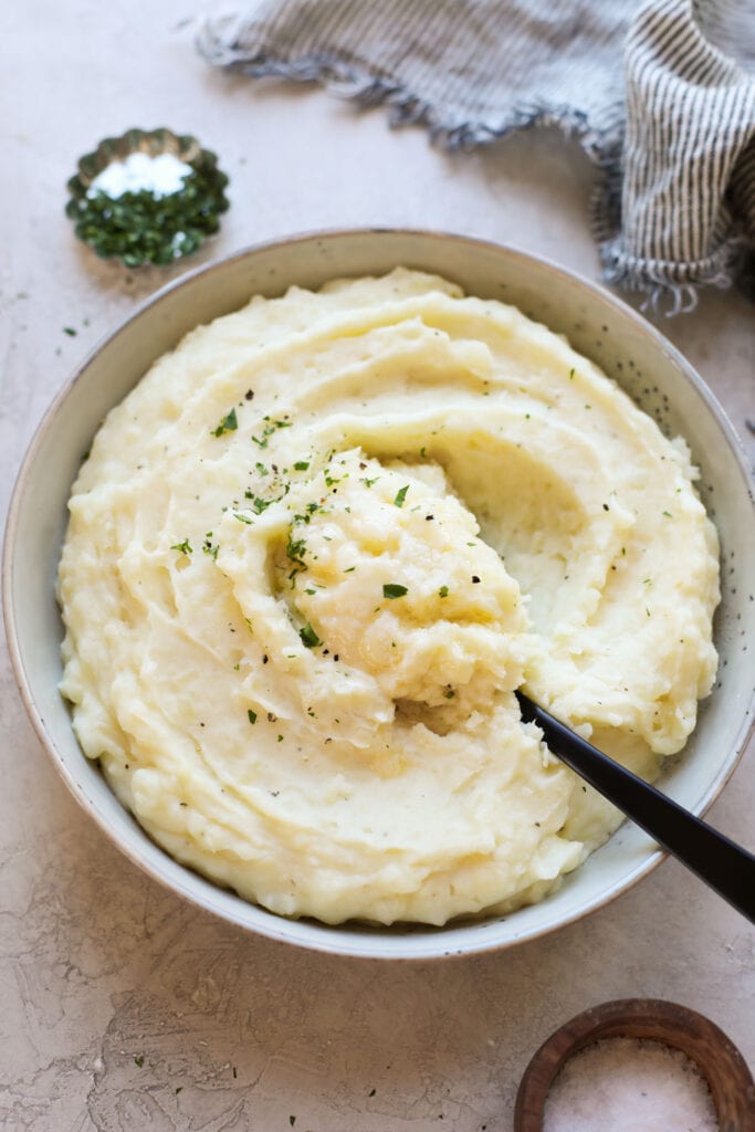 Close up view of a bowl of mashed potatoes with a black spoon scooping into the top. 