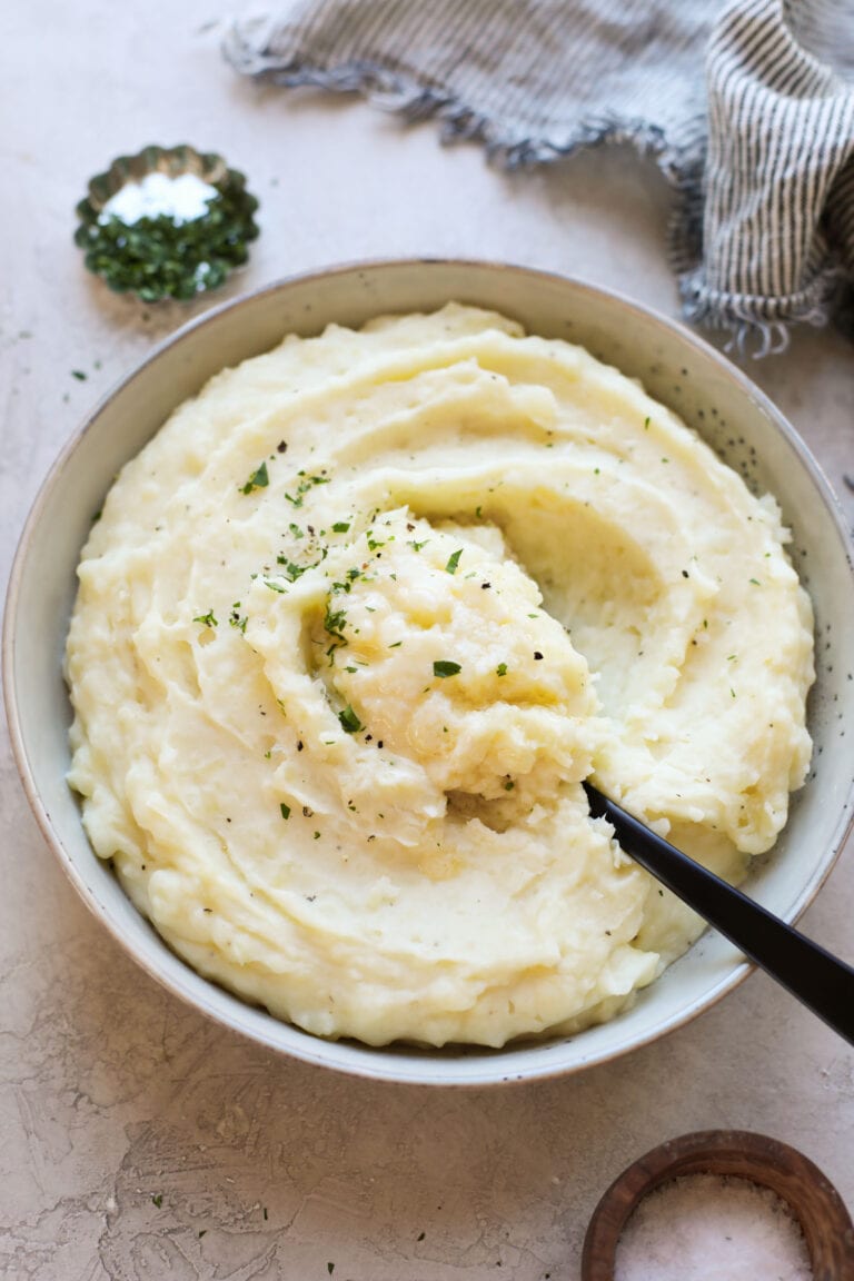 Overhead view of a bowl of mashed potatoes topped with melted butter and fresh herbs. 