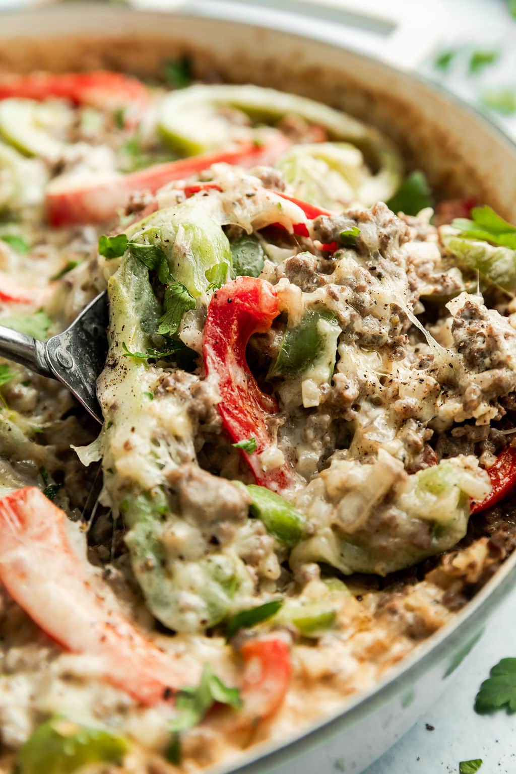 Fully cooked Low Carb Philly Cheesesteak Casserole being scooped with metal spoon out of a white skillet. 