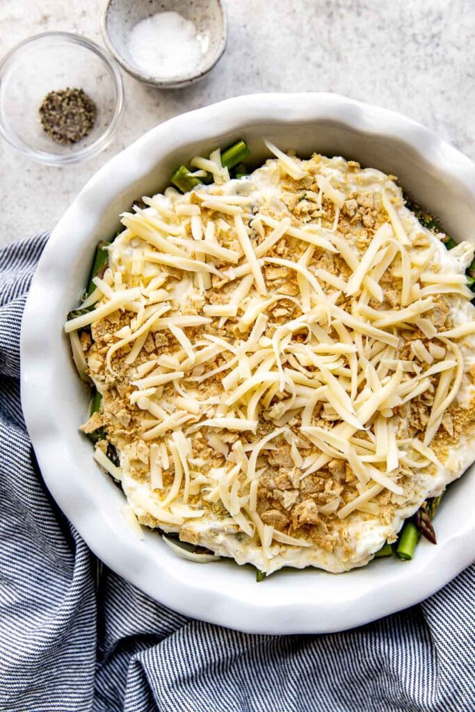 White dish with unbaked asparagus casserole topped with shredded cheese.