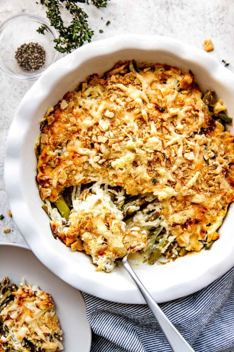 Overhead view of a freshly baked asparagus casserole topped with crushed crackers and melted Swiss cheese being scooped with a large metal spoon. 