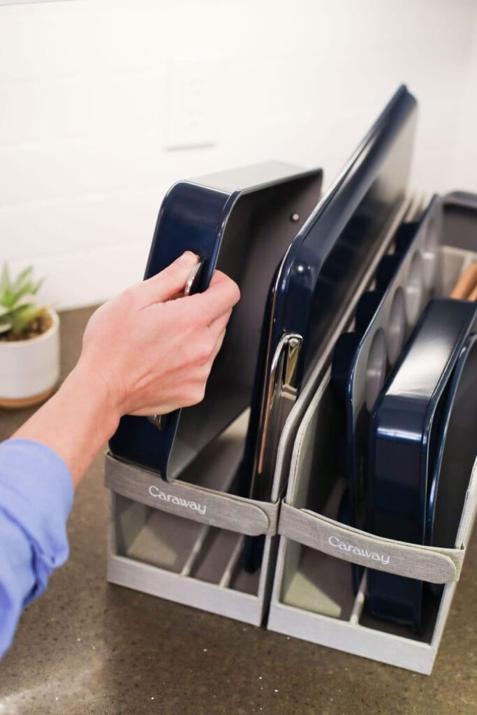 Hand reaching out to grab a caraway bakeware pan from the storage organizer. 