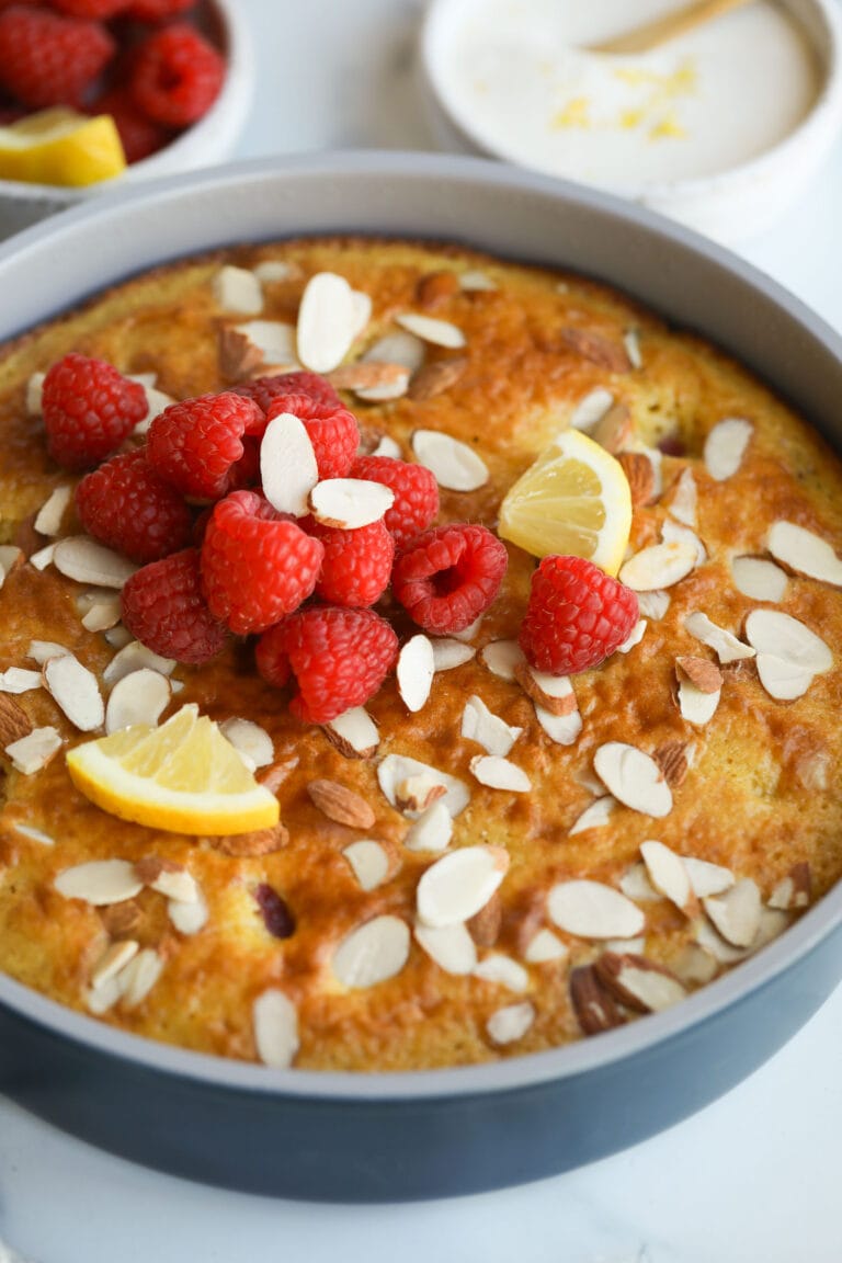 Close up view of a freshly baked raspberry lemon coffee cake topped with slivered almonds and fresh raspberries. 