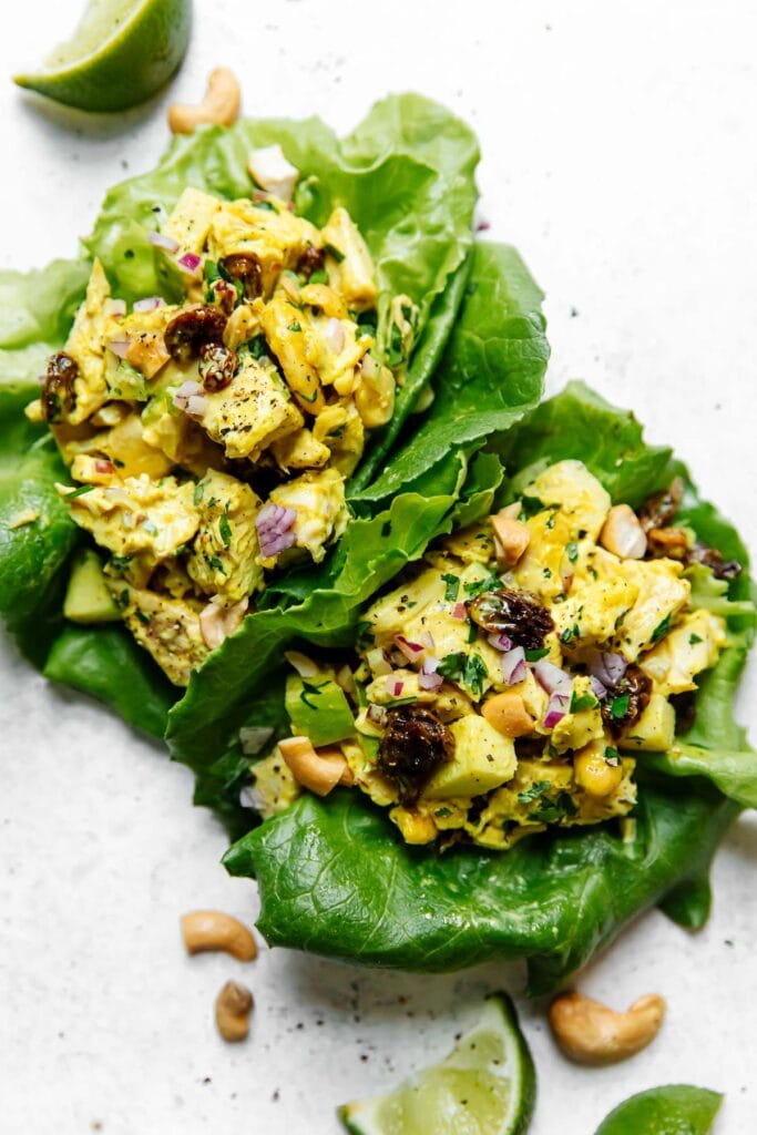 Two lettuce-wrapped scoops of curry chicken salad garnished with cashews and cilantro. 