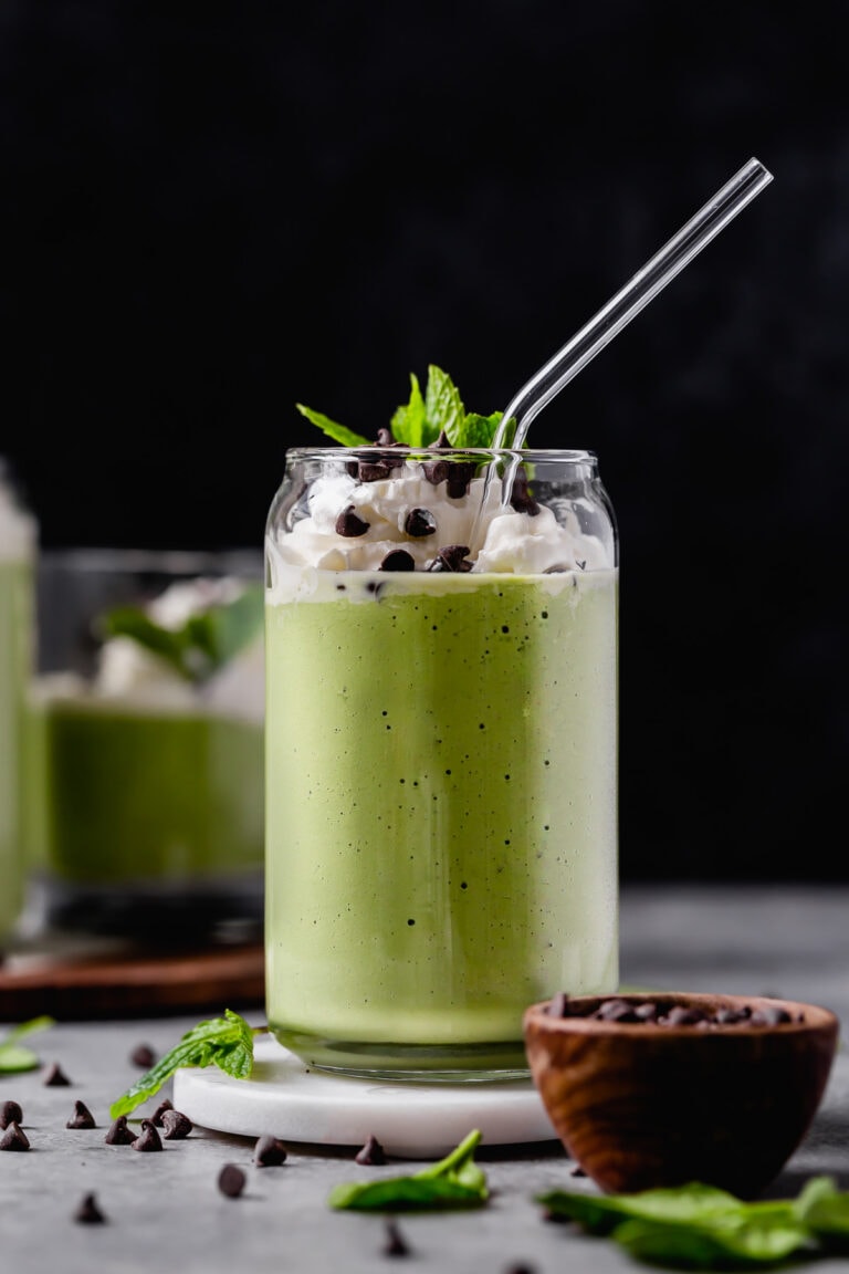 Close up view of a shamrock mint shake in a glass topped with whipped cream, chocolate chips and fresh mint.