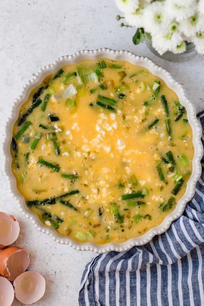 An asparagus quiche topped with feta in white pie plate