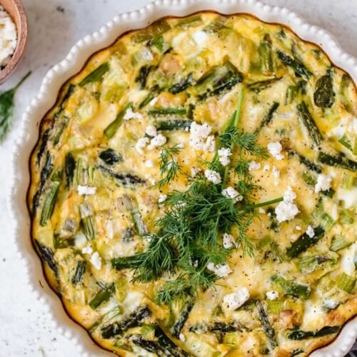 Overhead view white pie plate filled with crustless quiche with asparagus, leek and feta