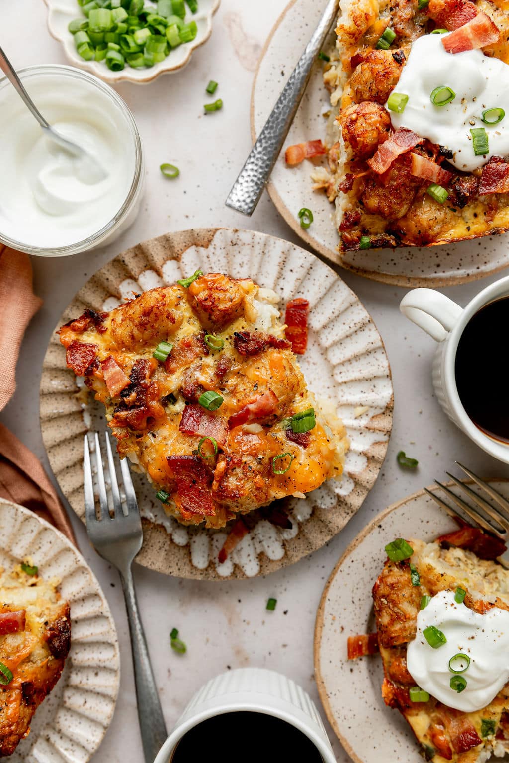 Overhead view of plated tater tot breakfast casserole topped with fresh herbs and surrounded by sour cream and green onions topping options.