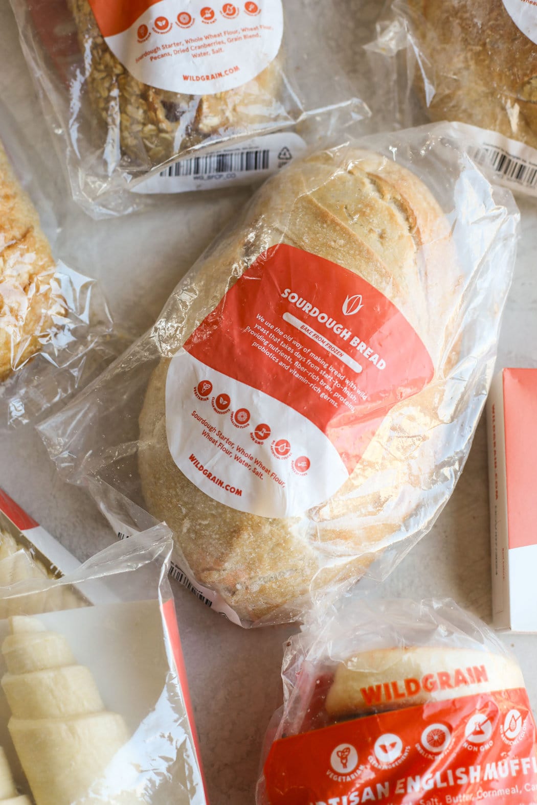 Overhead view of a sourdough bread loaf in a plastic bag, surrounded by additional baking products. 