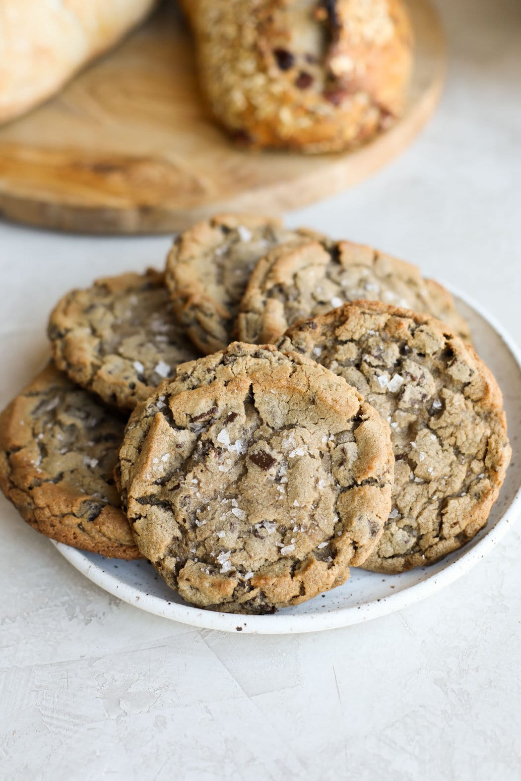 Close up view of fresh baked sourdough cookies on a white plate topped with flakey sea salt.