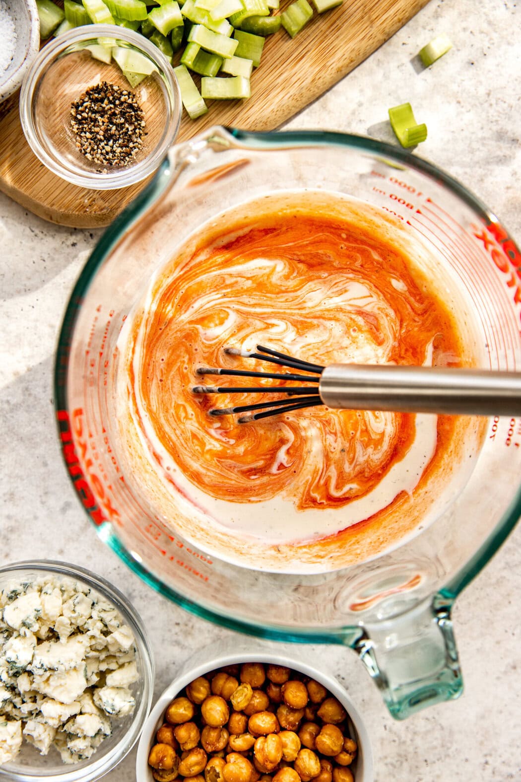 Overhead view of creamy dressing being whisked in a large glass measuring bowl. 