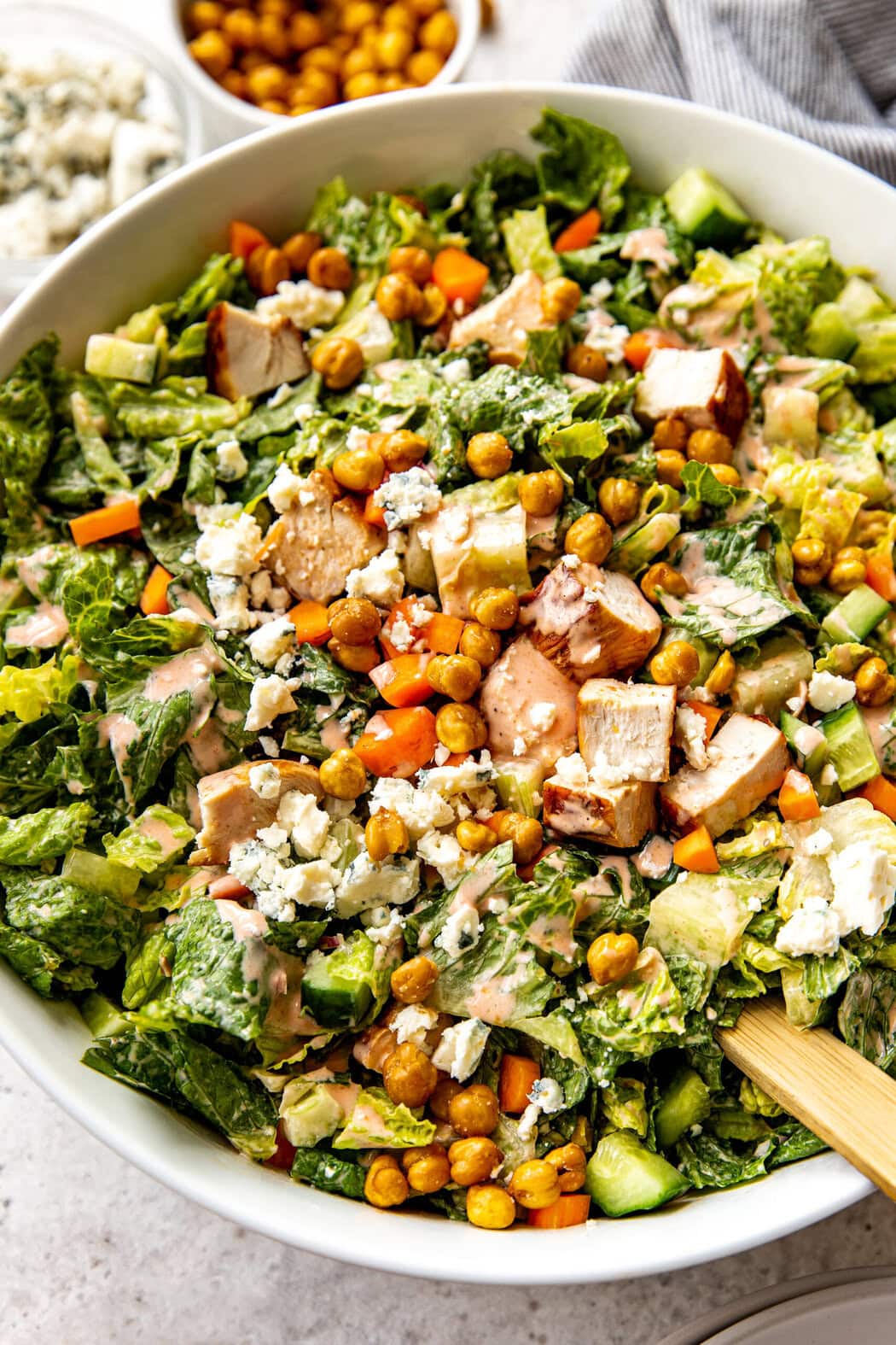 Close up view of a freshly tossed buffalo chicken salad topped with roasted chickpeas and crumbles of blue cheese. 