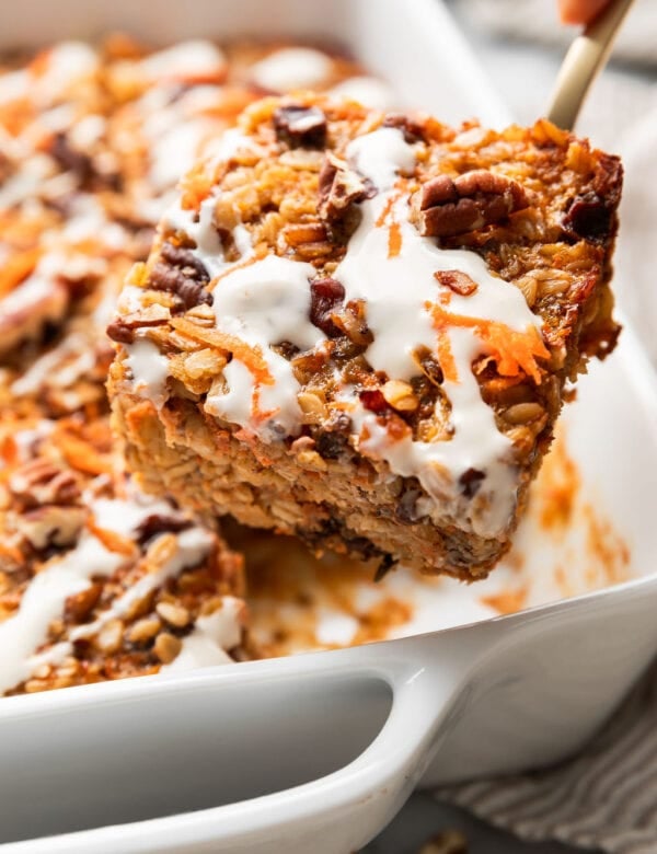 A serving of carrot cake baked oatmeal with cream cheese drizzle on top being removed from the pan.