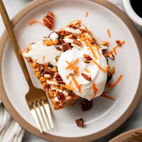 Close up view of a piece of carrot cake baked oatmeal topped with cream cheese drizzle, chopped pecans, and shredded carrots.