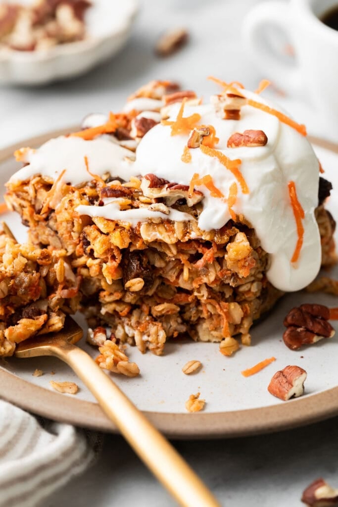 Close up view of a piece of carrot cake baked oatmeal topped with cream cheese drizzle, chopped pecans, and shredded carrots. 